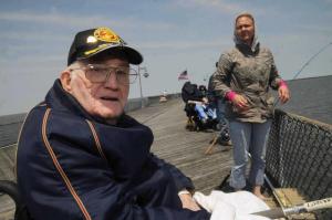 Marine Corps World War II veteran Ed Newman tries to keep his hands warm in the cool breeze while volunteer Jean Holdsworth-Steiner helps with the fishing gear. BY STEVEN BILLUPS