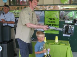 DNREC Sec. Collin O'Mara walks Andrew Wertz, 6, of Lewes, back to his parents. Wertz holds two trophies he won for his fishing skills. BY RACHEL SWICK MAVITY