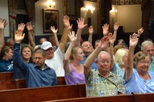 Some of the more than 70 opponents of the application raise their hands during the July 10 public hearing. BY RON MACARTHUR