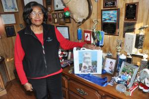 Janie Miller poses next to her family's wall of awards and recognitions. BY NICK ROTH
