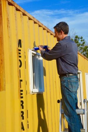Homes of Hope Executive Director Lance Manlove applies caulk to a window on a container home prototype being constructed in West Rehoboth. BY RON MACARTHUR
