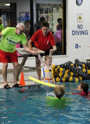 YMCA aquatics coordinator Lydia Schmierer, right, and volunteer John Zinsmeister assist Kage Wilke with his entry into the pool. BY DAN COOK