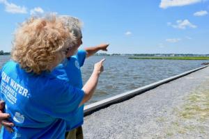 Tom and Barbara Shamp point to their orange-roofed home across the water. MADDY LAURIA PHOTO