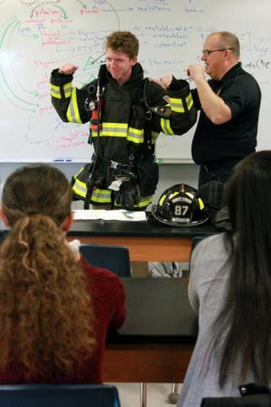 To illustrate the physical demands of his job, EMT/firefighter and Seaford Volunteer Fire Department Pastor Larry Whaley has student Logan Tyler don firefighter gear including a tank and full-face mask.
