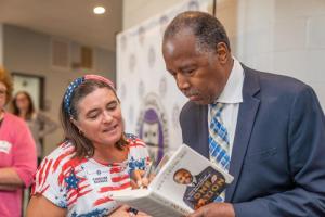 Dr. Ben Carson, right, autographs a copy of "Why America Matters" for Caroline Schneck, DCS middle school teacher.