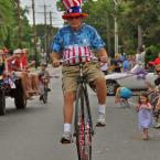 Jim Powell towers over the parade route riding an antique high-wheel bicycle. BY RON MACARTHUR