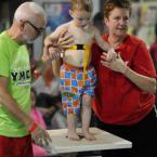Volunteer John Zinsmeister, left, and YMCA aquatics coordinator Lydia Schmierer assists Kage Wilke, 2, with his entry into the pool. BY DAN COOK